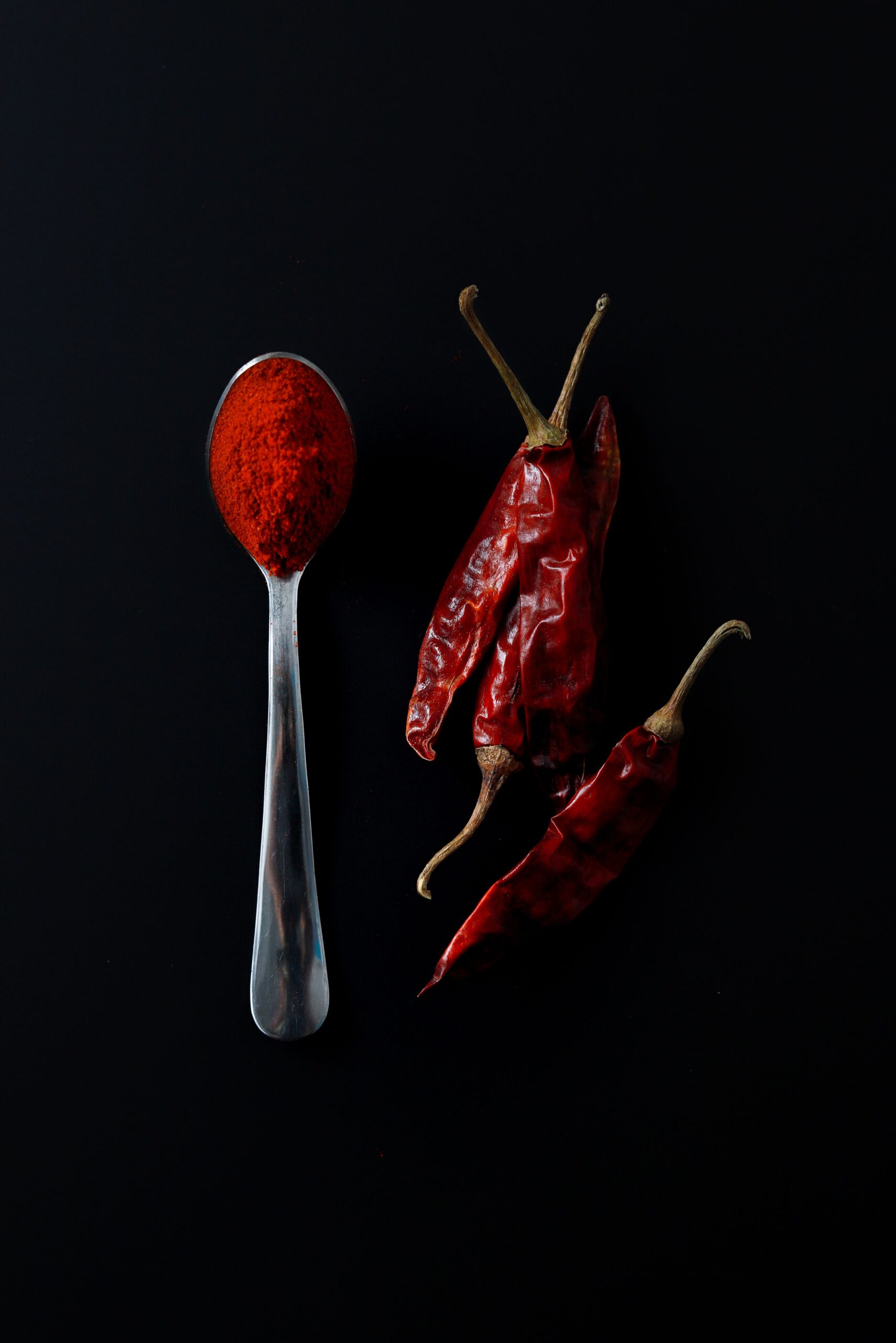 Chiles rojos secos junto a una cuchara de chile molido sobre fondo oscuro